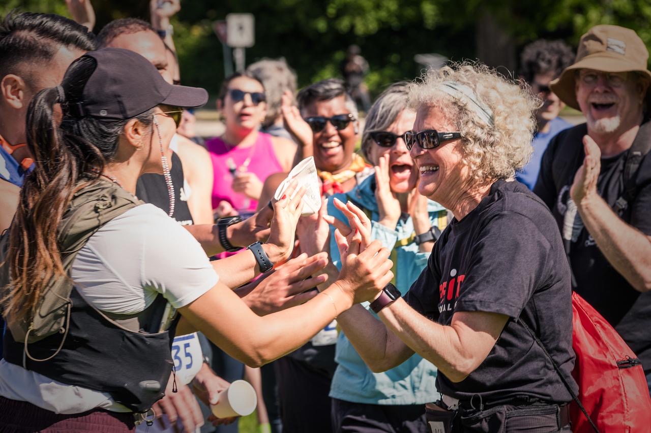 Two Striderz run club women high-fiving in a crowd with trees and people in the background