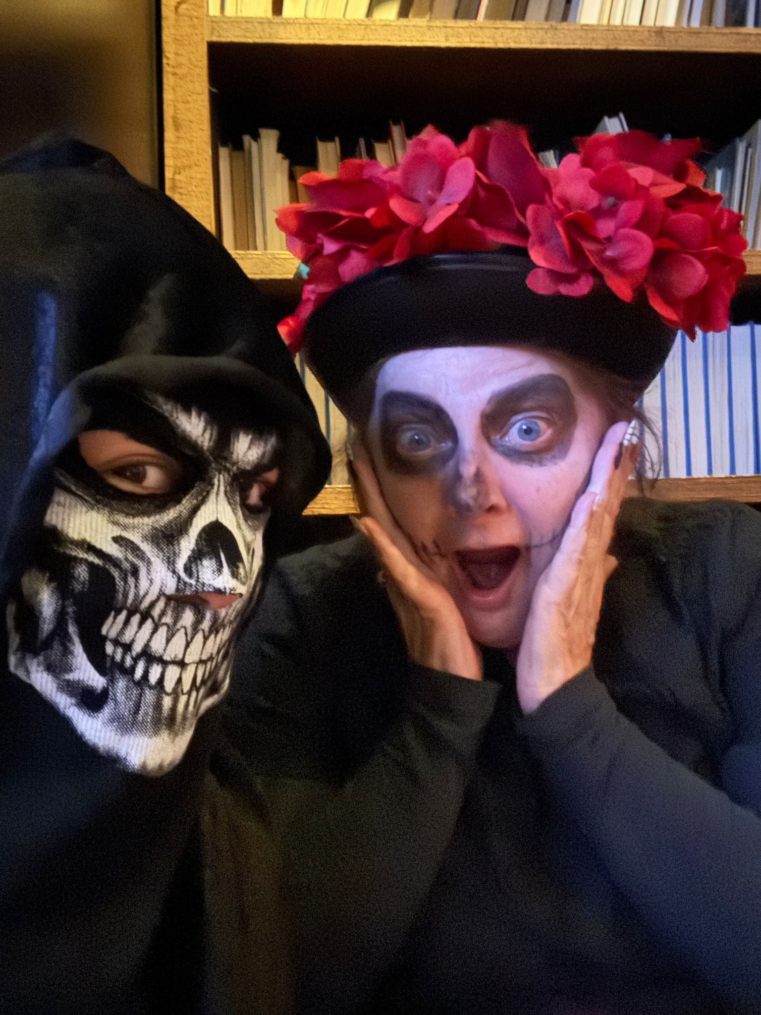 Two people wearing Halloween-themed makeup and costumes in front of a bookshelf.
