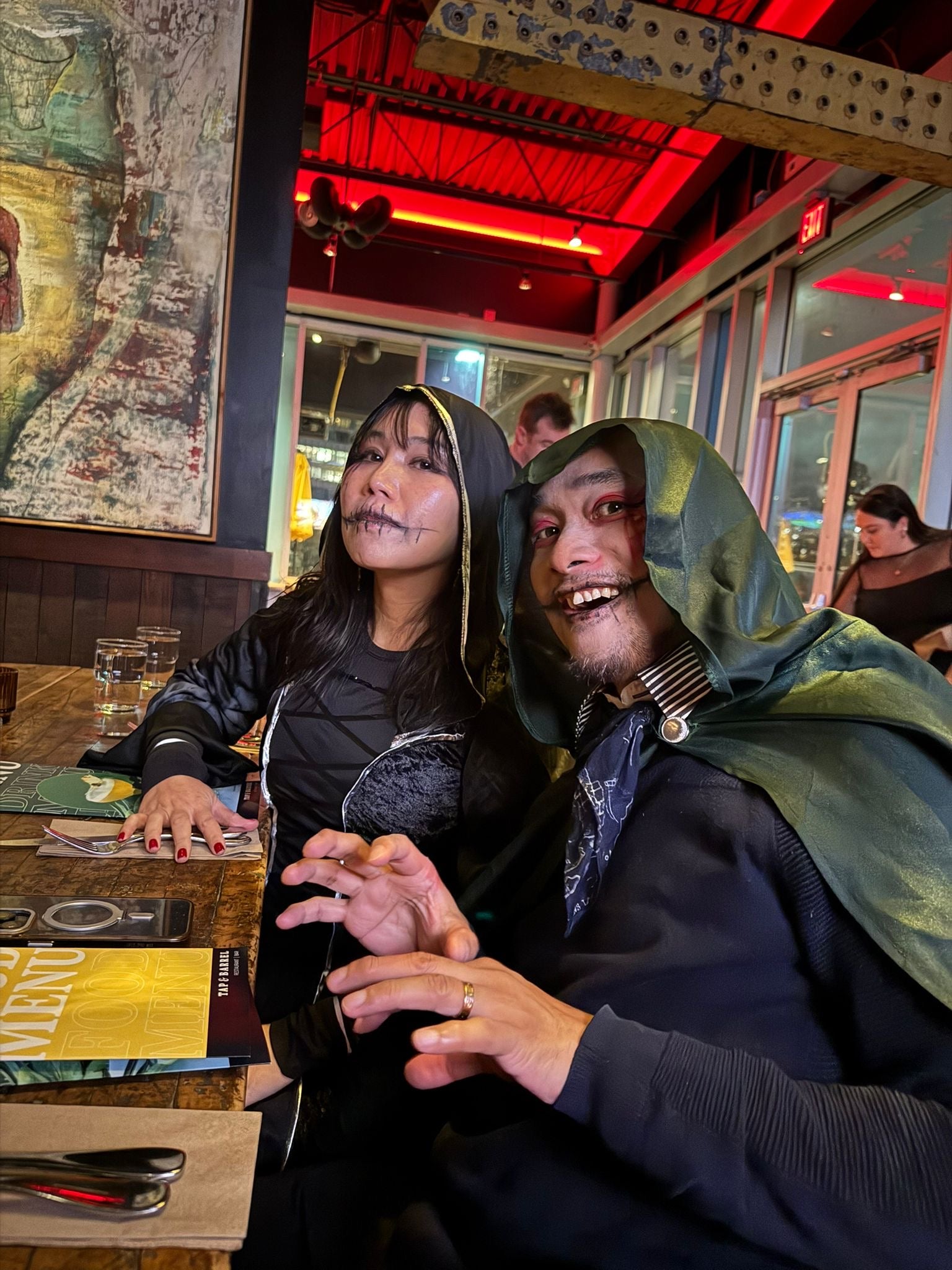 Two people in costumes sitting at a table in a restaurant with red lighting.