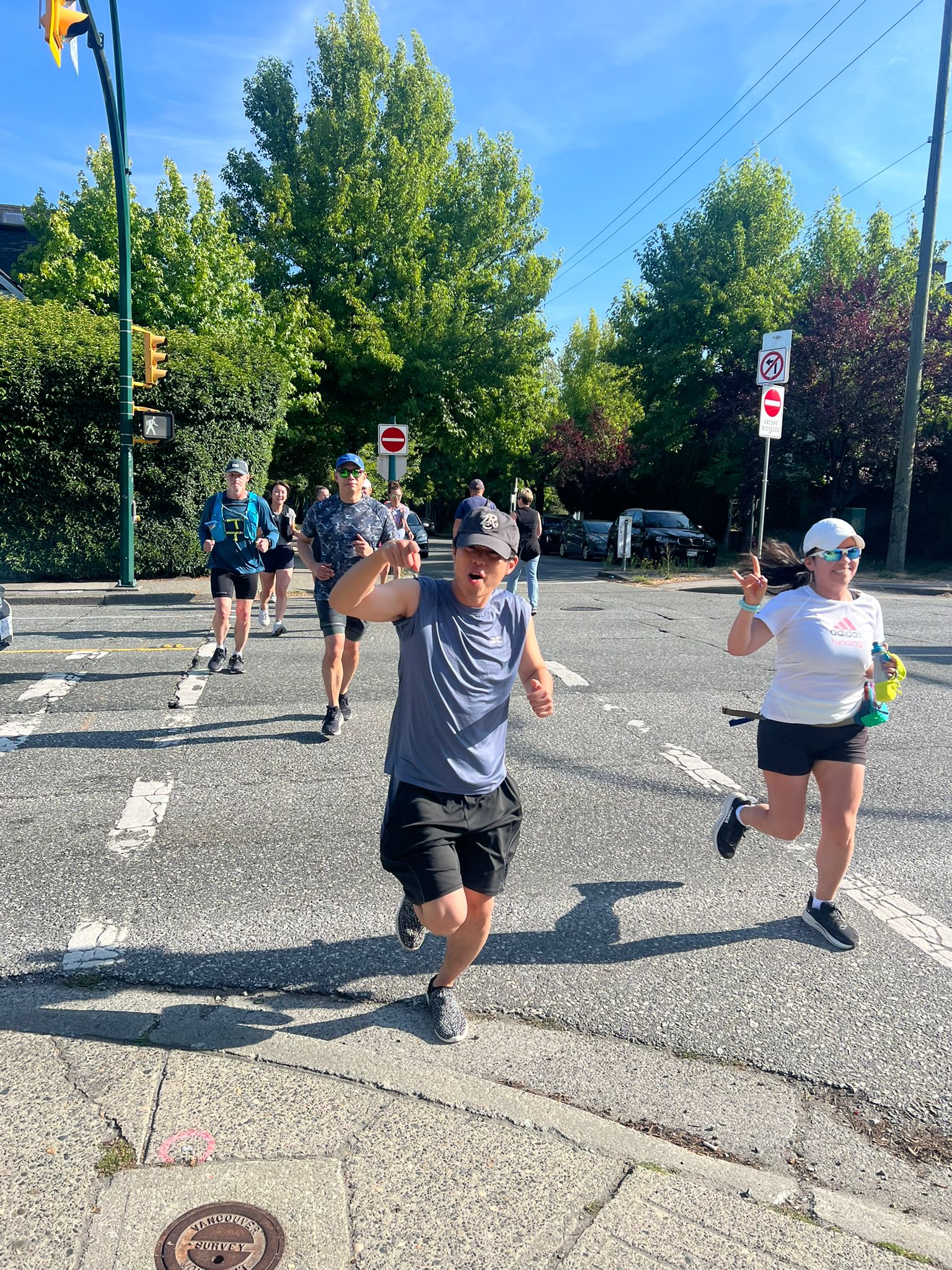 Striderz Run club runners crossing a street on a sunny day with trees and traffic lights in the background.