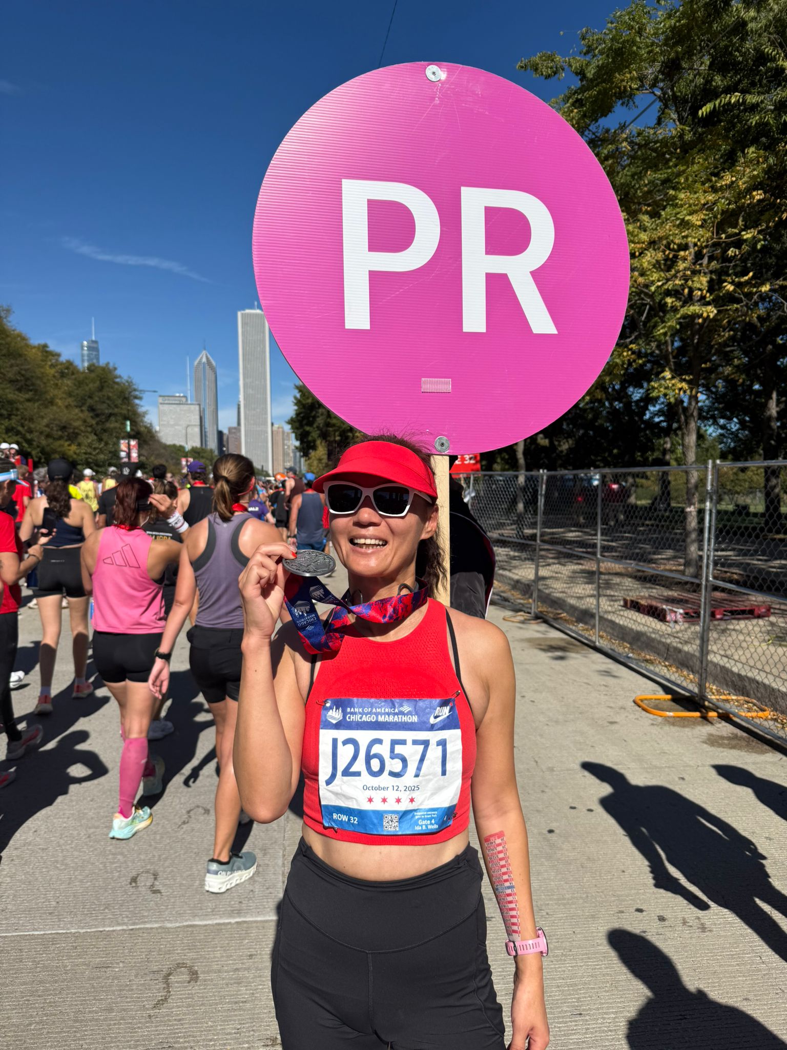 Runner holding a pink 'PR' sign during a race with a city skyline in the background.