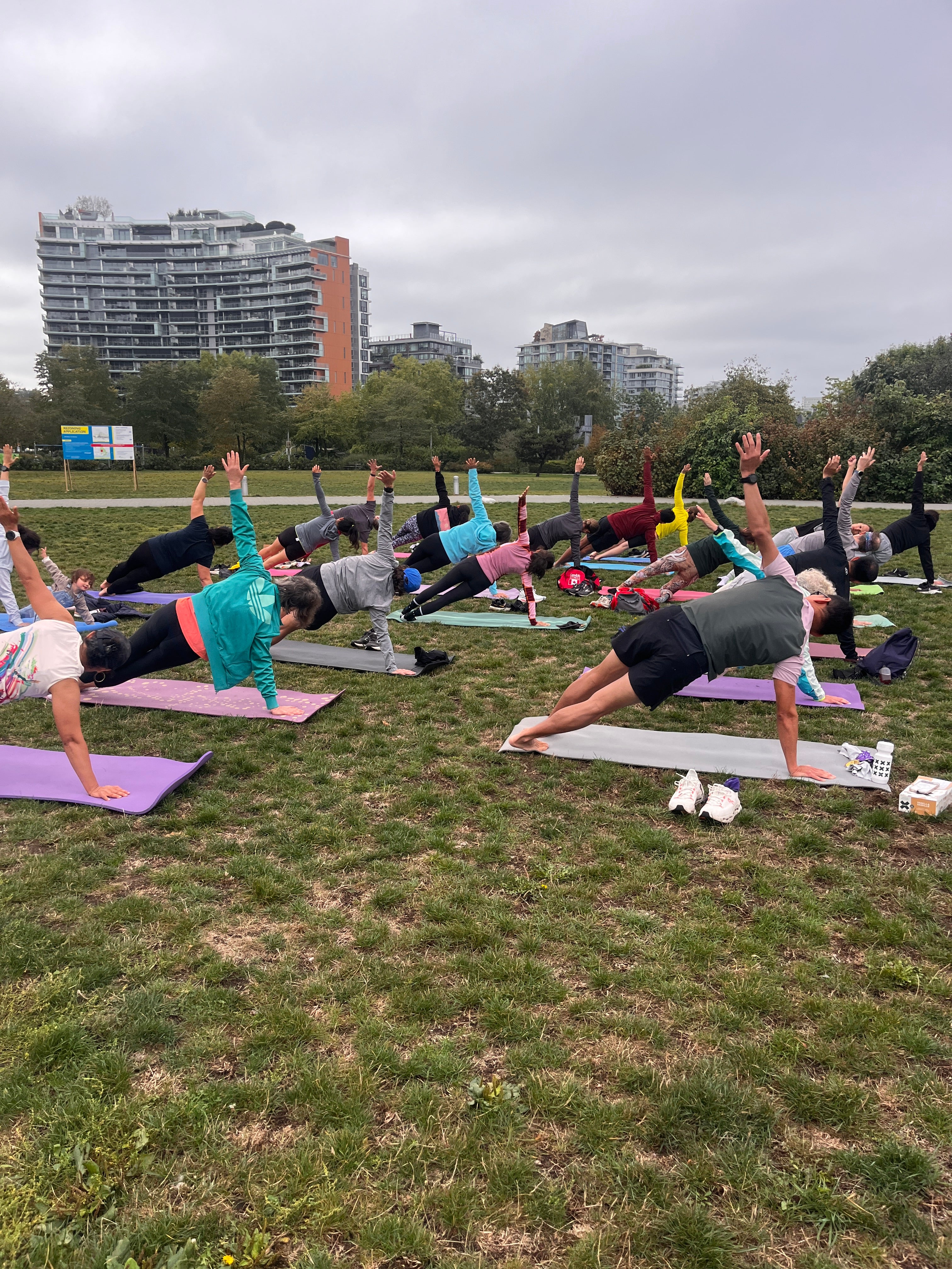 Group of Striderz run club runners participating in a yoga activity on a grassy field with buildings in the background.